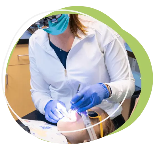 LipTongueTies (1) A dentist wearing a mask and gloves examines a patient's mouth using dental tools. The patient is lying back and wearing protective glasses.