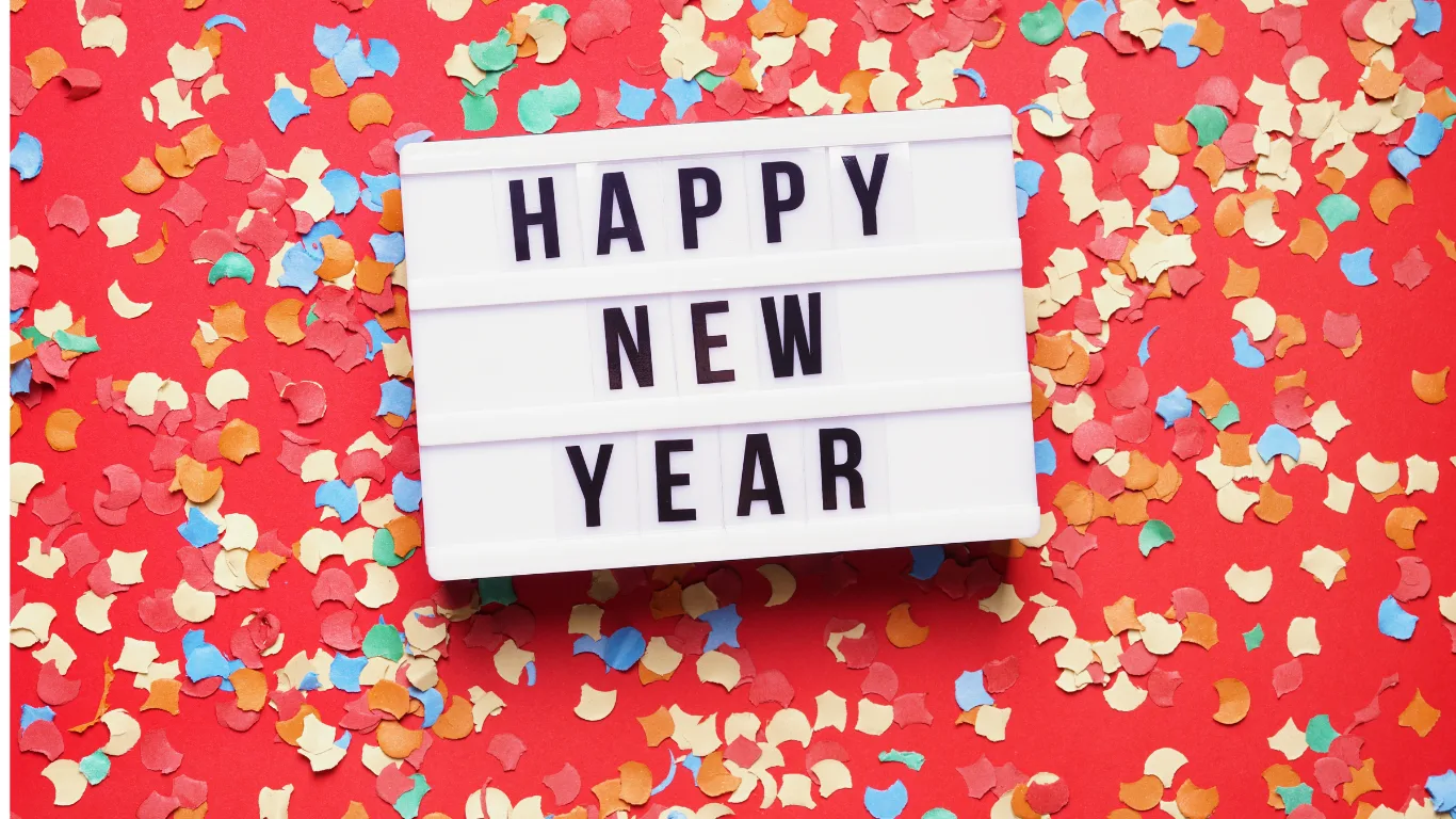 A lightbox sign with the words "HAPPY NEW YEAR" is placed on a red background covered with colorful confetti.